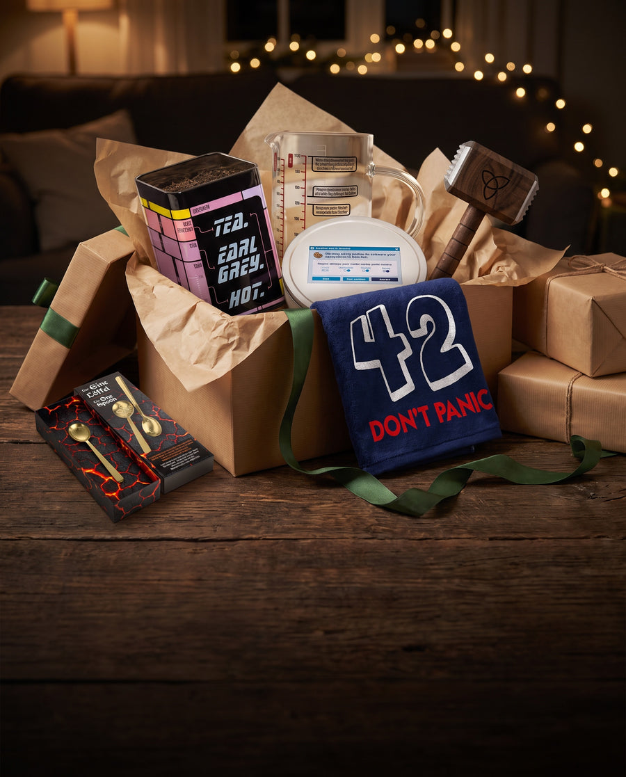 Geöffnete Geschenkbox mit Teedose „Tea. Earl Grey. Hot.“, Messbecher, Keksdose „Accept Cookies“, Mjölnir-Fleischhammer, Badehandtuch 42 und Der EINE Löffel
